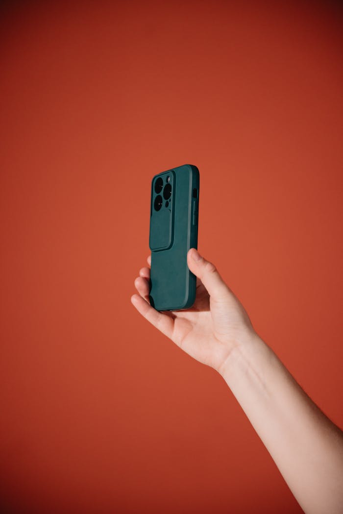 Close-up of a hand holding a smartphone with a red background, showcasing modern technology.